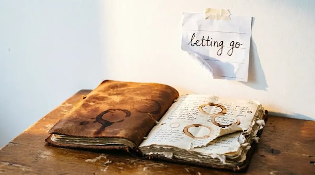 Coffee-stained notebook open with multiple coffee rings on desk below torn letting go note on wall morning light(AI-generated illustration)