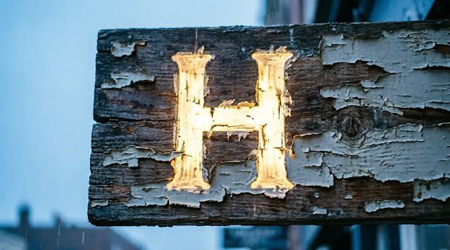 Glowing letter H on weathered sign, peeling paint reveals hidden name, twilight (AI-generated illustration)