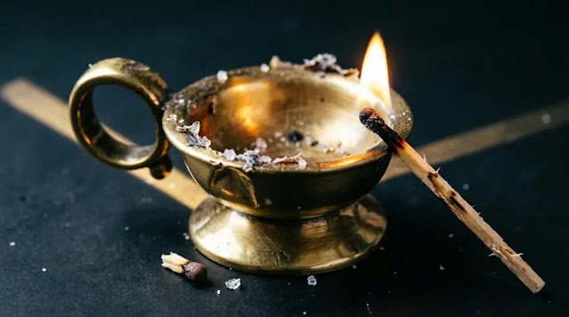 Brass votive with struck match leaning on rim, tiny flame illuminates path. (AI-generated illustration)