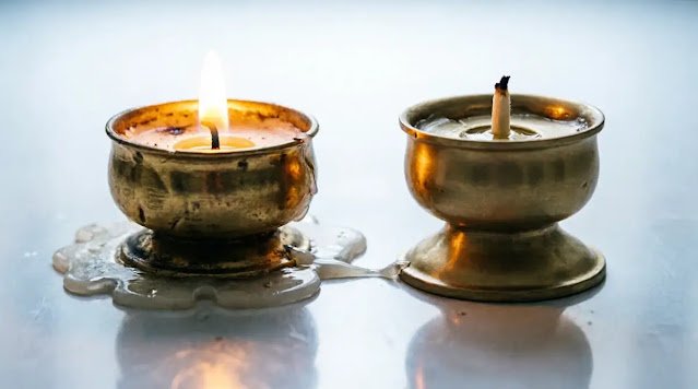 Brass votive with flame beside fresh identical holder, reflection shows both burning. (AI-generated illustration)